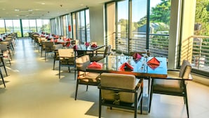 A spacious dining area with tables set for guests, large windows offering views of the outdoors, and a clean, modern interior design. - K Hotels (Entebbe)