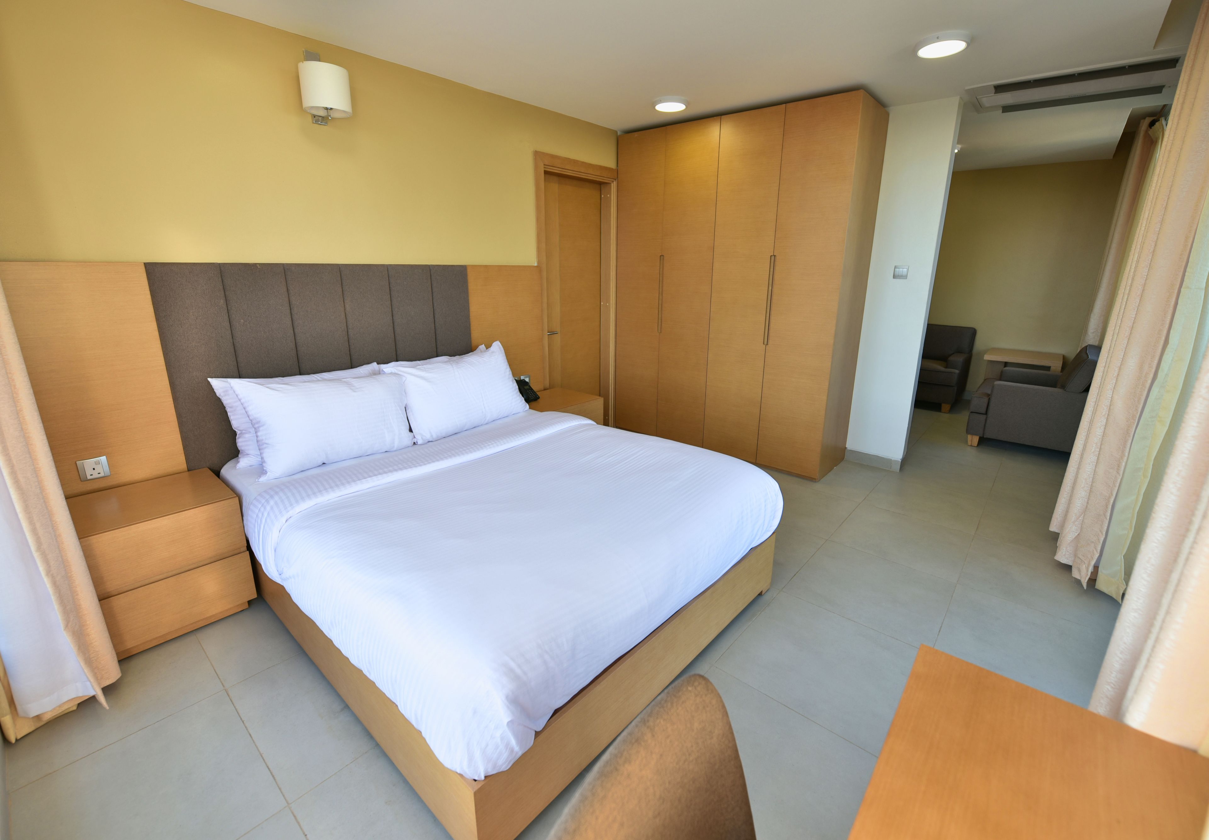 A hotel room with a large bed, wooden wardrobe, and a small seating area.