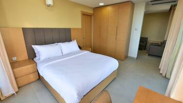 A hotel room with a large bed, wooden wardrobe, and a small seating area.