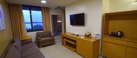 A hotel room with a sofa, a small desk, a flat-screen TV, and a view of the outdoors.