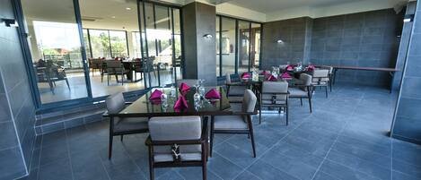 A modern dining area with glass walls, dark tiled floors, and neatly arranged tables with chairs.