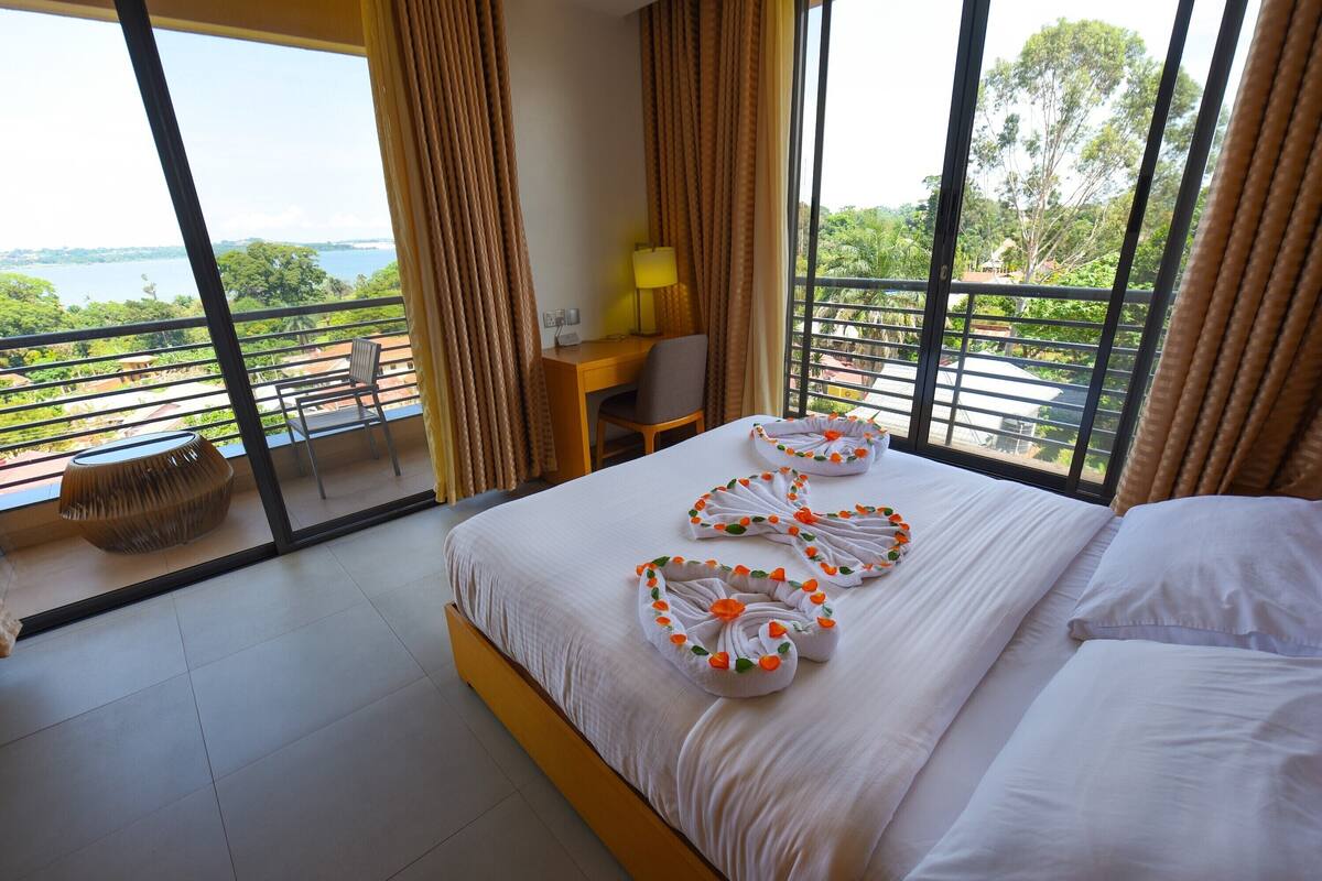 Habitación de hotel con una cama grande, un escritorio, una silla y vistas a un cuerpo de agua y vegetación.