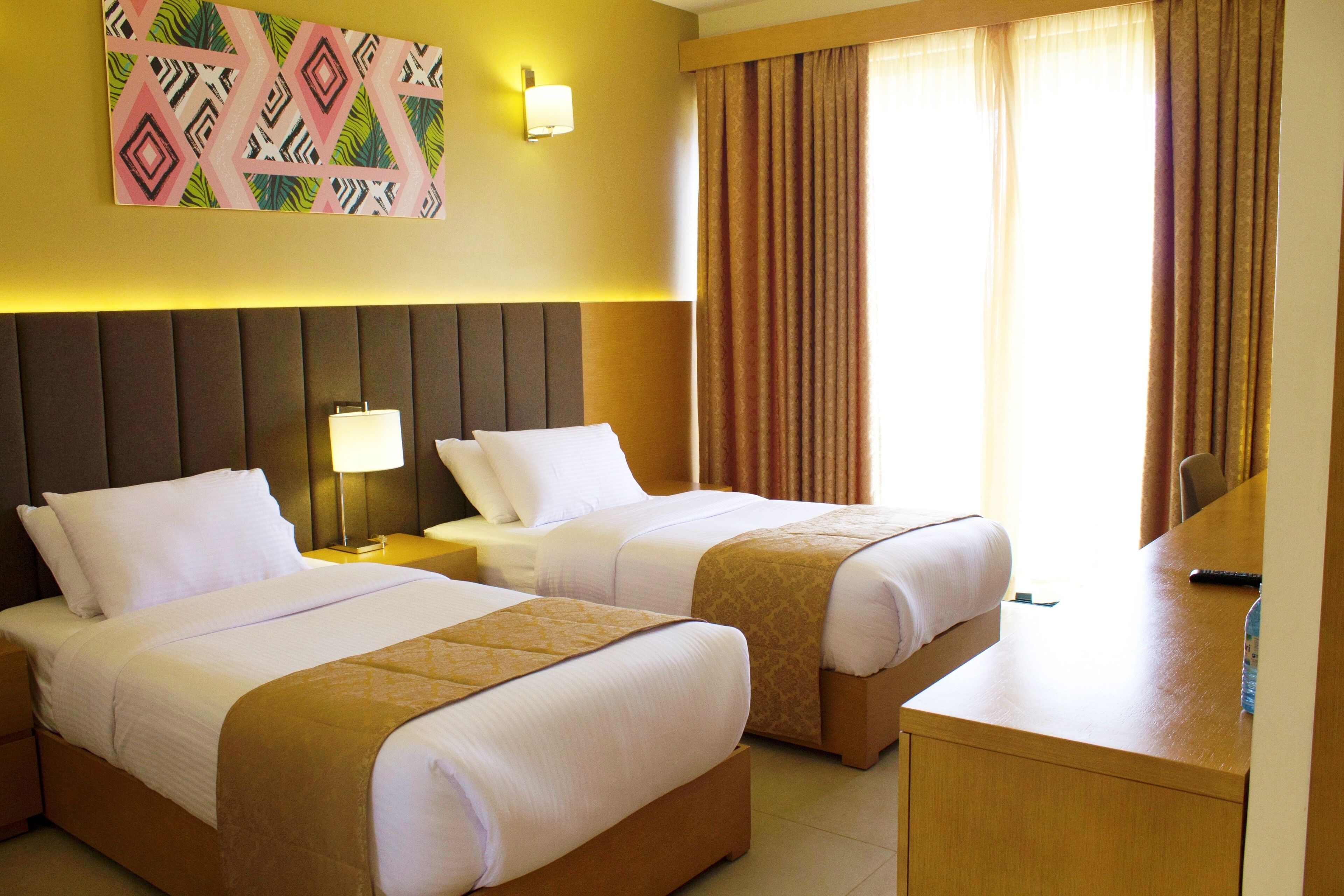 A hotel room with two beds, a desk, a lamp, and a painting on the wall.