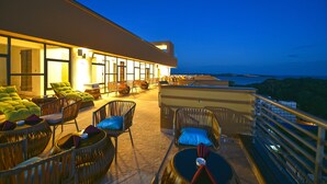 A rooftop terrace with wicker furniture and a view of the ocean at dusk. - K Hotels (Entebbe)