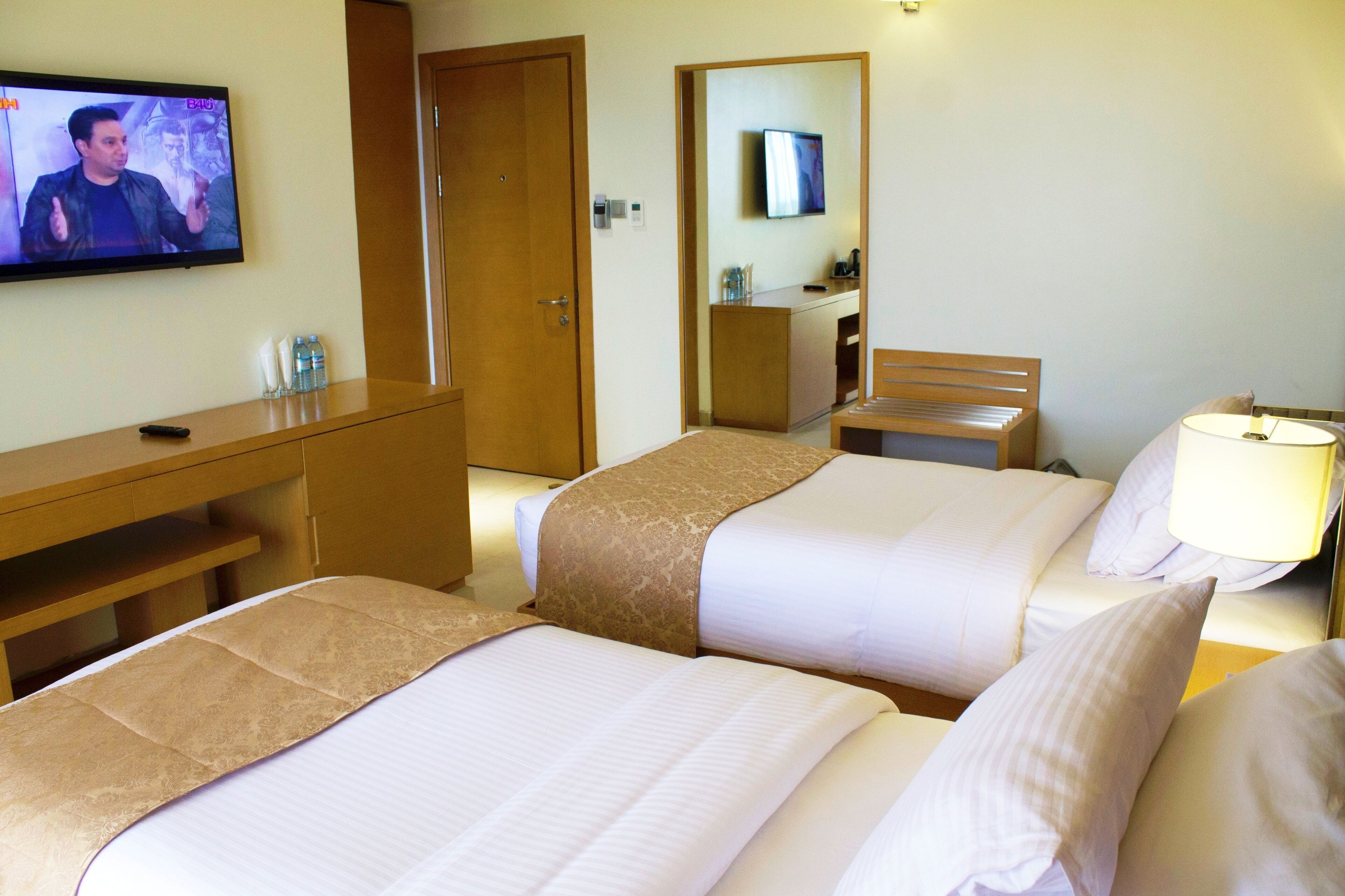 A hotel room with two beds, a desk, a TV, and a mirror.