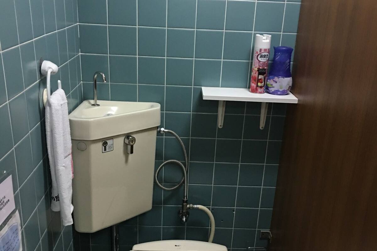 A small bathroom with a toilet, sink, and shower. There is a shelf with toiletries and a towel rack.