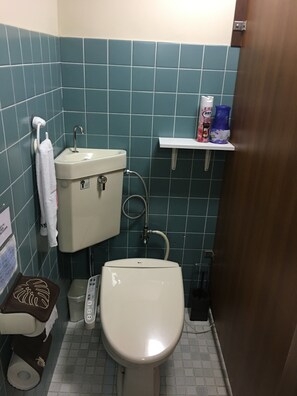 A small bathroom with a toilet, sink, and shower. There is a shelf with toiletries and a towel rack. - Guest Inn Chita (Kyoto)