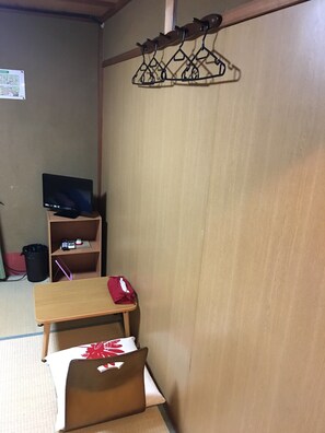 A room with a wooden desk, a television on a stand, a shelf with electronic devices, and a hanging clothes rack. - Guest Inn Chita (Kyoto)