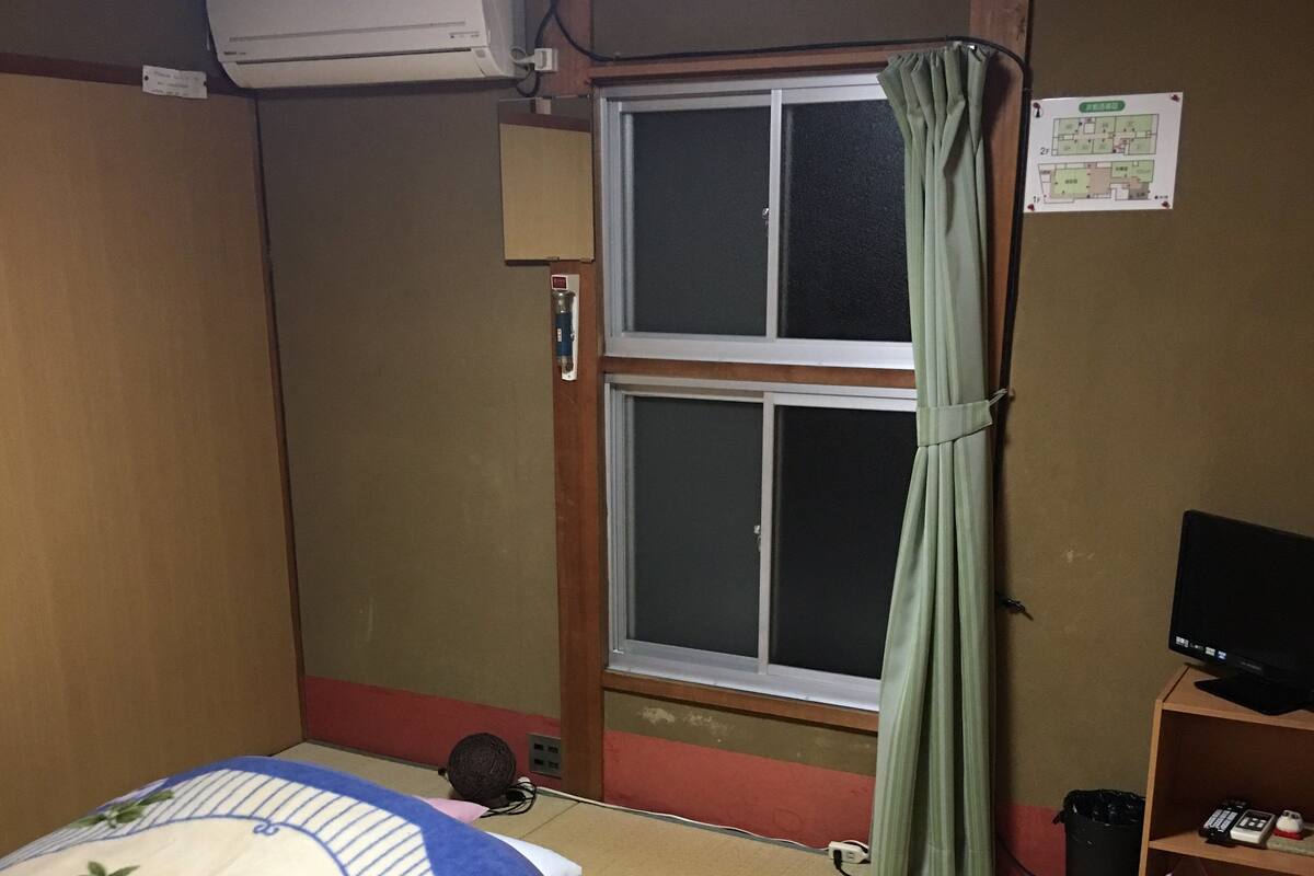 A room with a bed, a small table, a television, and a window with a curtain.