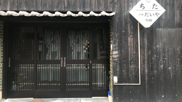 Ein traditionelles japanisches Gebäude mit einem schwarzen Tor und einem Schild, das ein Gasthof anzeigt.