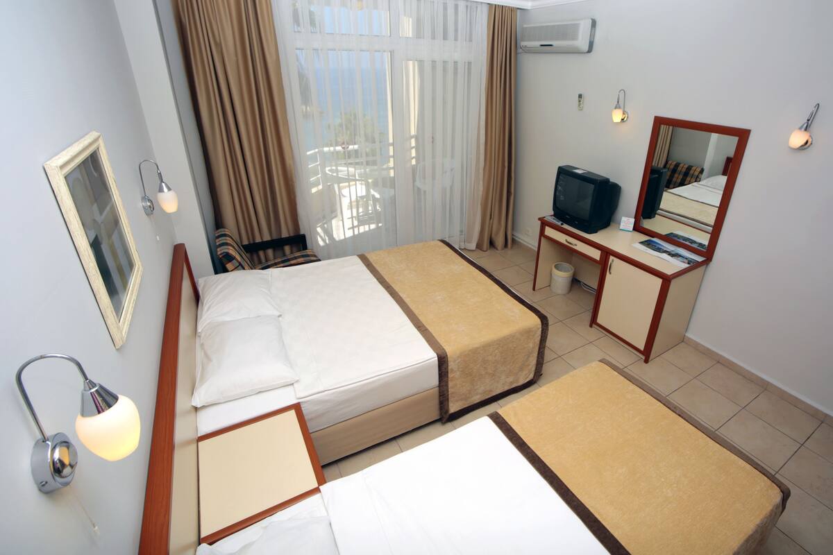 A hotel room with two beds, a desk, a television, a mirror, and a window with curtains.