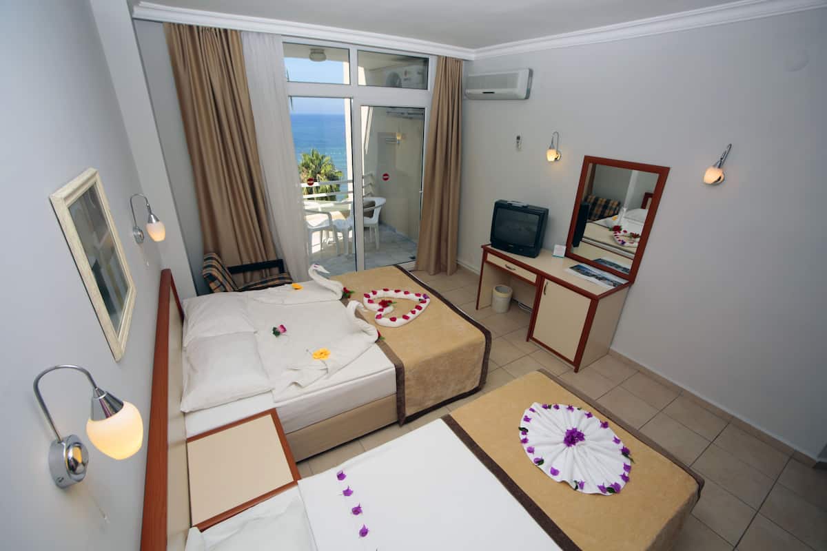 A hotel room with a bed, a desk, a TV, and a balcony with a view of the sea.