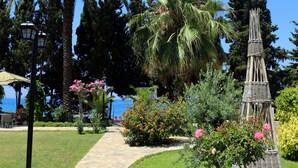 A stone pathway leading through a garden with palm trees, a wicker gazebo, and a view of the sea. - Incekum Su Hotel - All Inclusive (Alanya)
