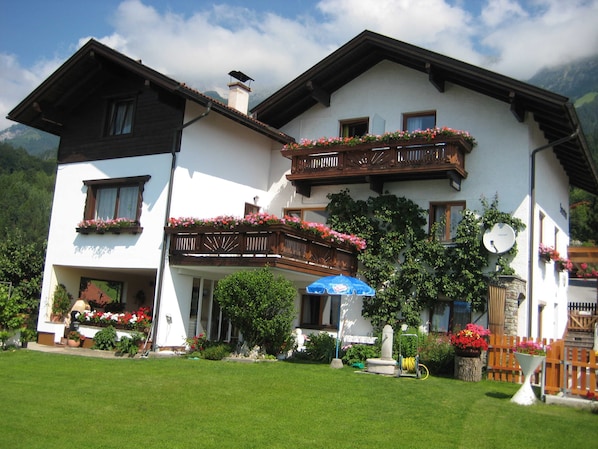 A two-story building with balconies, a garden, and a mountain backdrop. - Single room with shower and toilet 3 - Gästehaus Sonnenheim (Thaur)