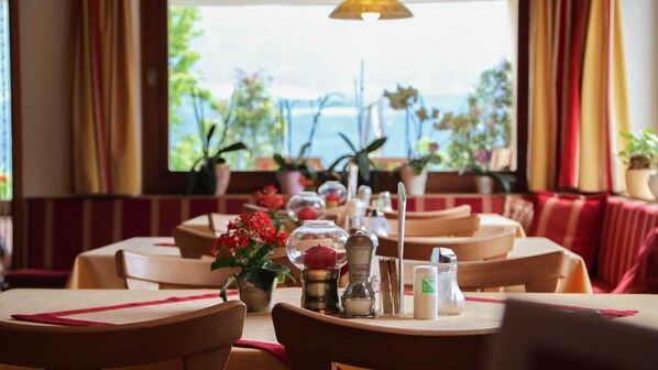 A restaurant with tables set for dining, potted plants, and a view of the sea.