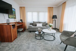 Une chambre d’hôtel équipée d’un canapé, d’une table basse, d’une télévision, d’une lampe et d’un bureau avec une lampe.
