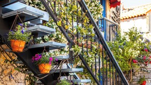 Ein Steinhaus mit einer schwarzen Metalltreppe, umgeben von verschiedenen Topfpflanzen.