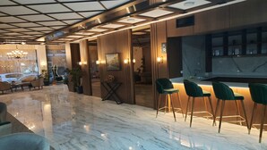 A modern lobby with a marble floor, wooden paneling, and a bar area with green bar stools. - Nadir Business Hotel (Karaman)