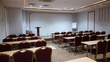 Uma sala de conferências com várias mesas e cadeiras, um pódio e uma tela de projeção.