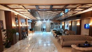 A spacious lobby with a marble floor, a reception desk, a sofa, and a television screen. - Nadir Business Hotel (Karaman)