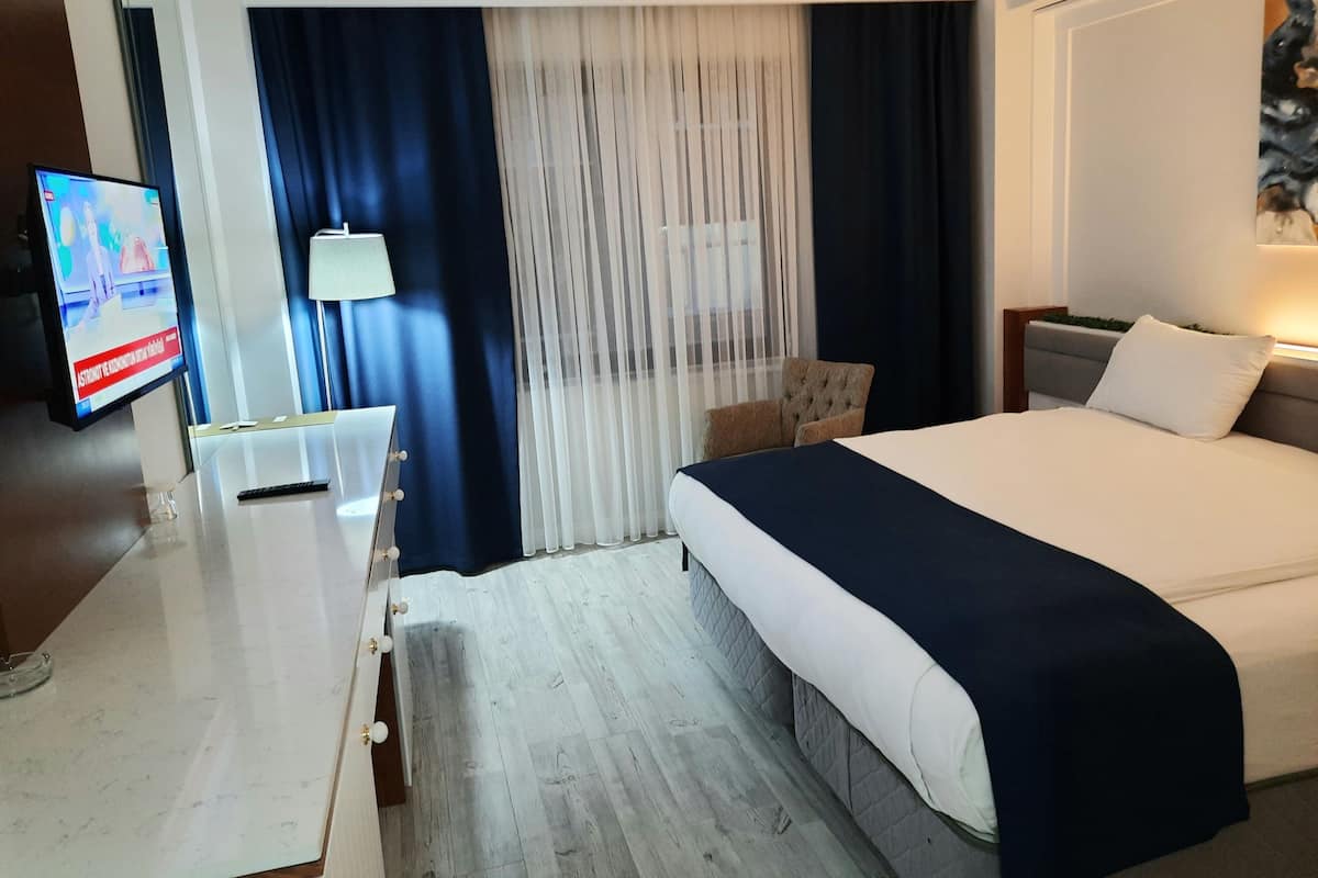 Une chambre d’hôtel avec un lit, un bureau doté d’une lampe, une chaise et un téléviseur diffusant un programme d’information.