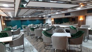 A modern dining area with multiple tables and chairs, a patterned ceiling, and a brick accent wall. - Nadir Business Hotel (Karaman)