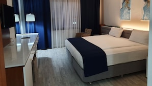 A modern hotel room with a large bed, a desk with a lamp, a chair, and artwork on the walls. - Nadir Business Hotel (Karaman)