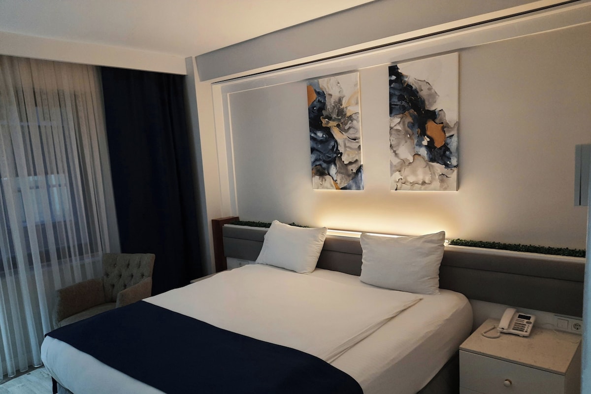 A modern hotel room with a large bed, bedside tables, and abstract wall art.