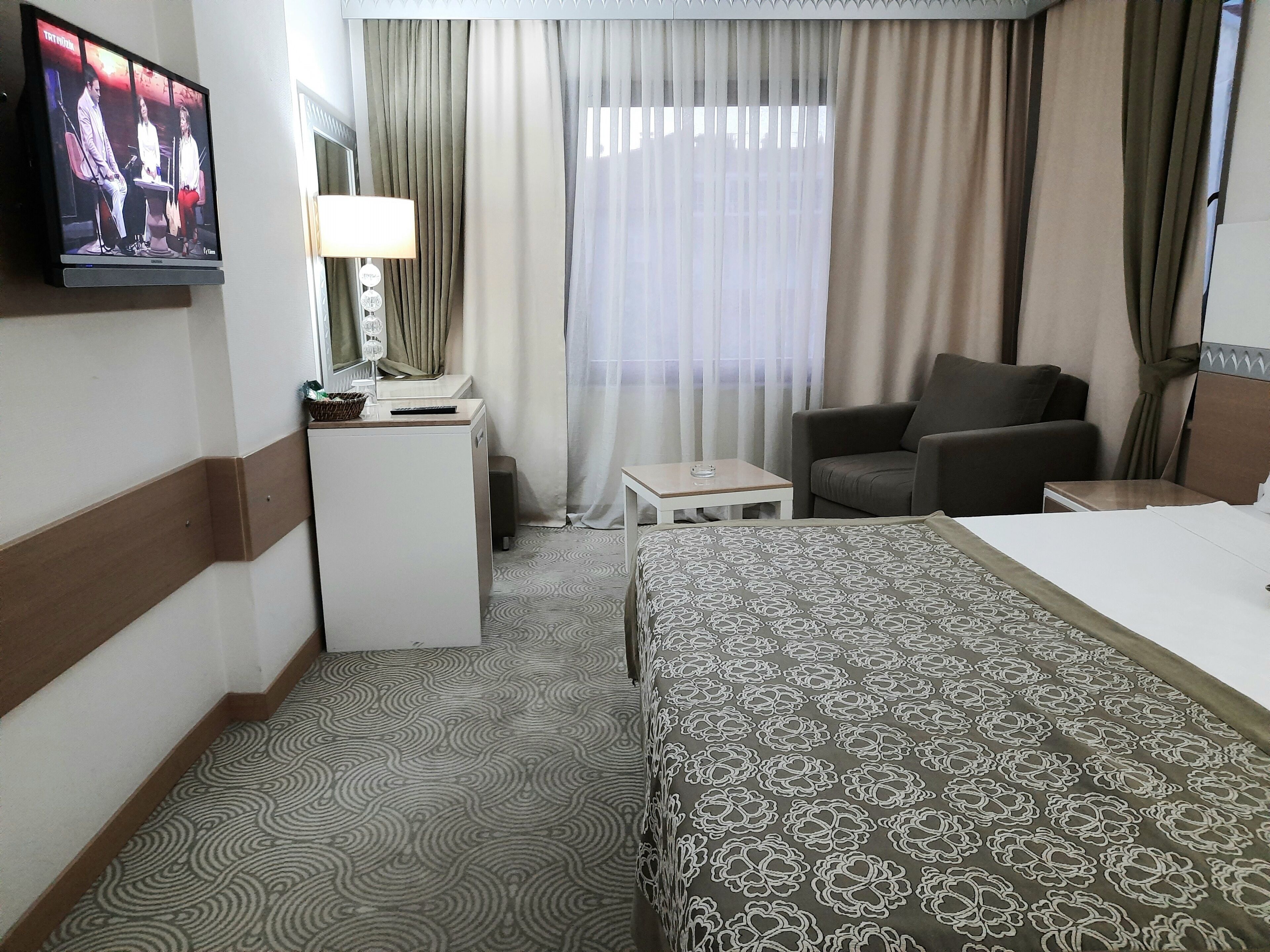 Una habitación de hotel con cama, escritorio, silla, televisor y ventana con cortinas.