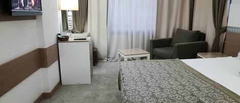 Una habitación de hotel con cama, escritorio, silla, televisor y ventana con cortinas.