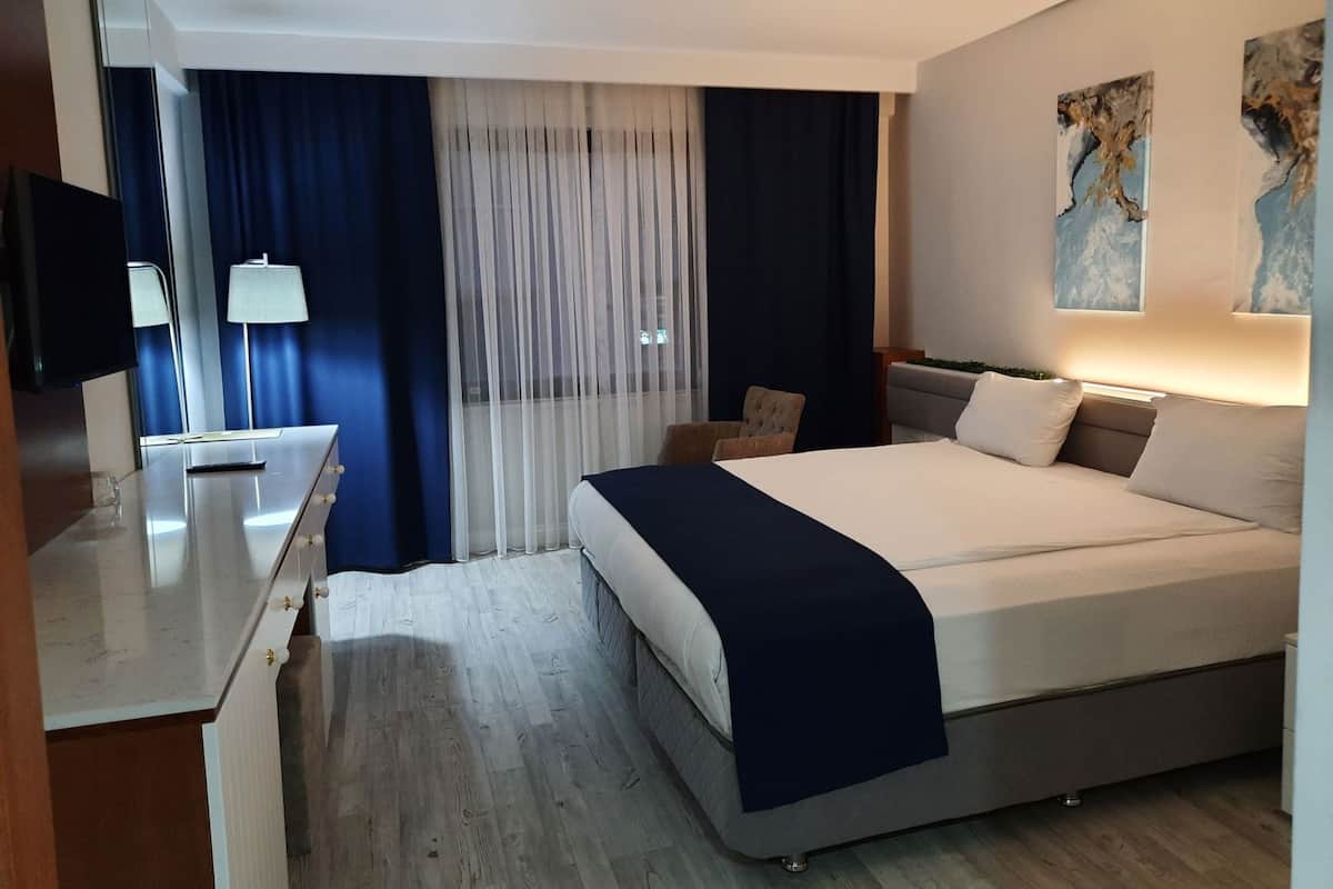 Une chambre d’hôtel avec un lit, un bureau, une chaise, une lampe et des œuvres d’art accrochées au mur.