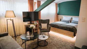 Una habitación de hotel con cama, televisor, sofá, mesa de centro y lámpara.
