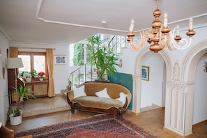 Une pièce avec un canapé, un lustre, un escalier et une grande plante.