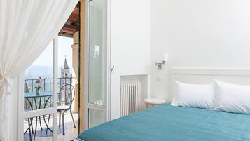 Un dormitorio con una cama grande, vista a una torre a través de una puerta de balcón, una mesita con sillas y un radiador.