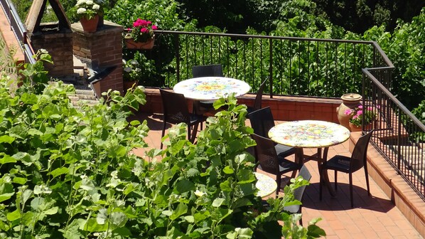An outdoor patio with two round tables and chairs, surrounded by lush greenery and potted plants.