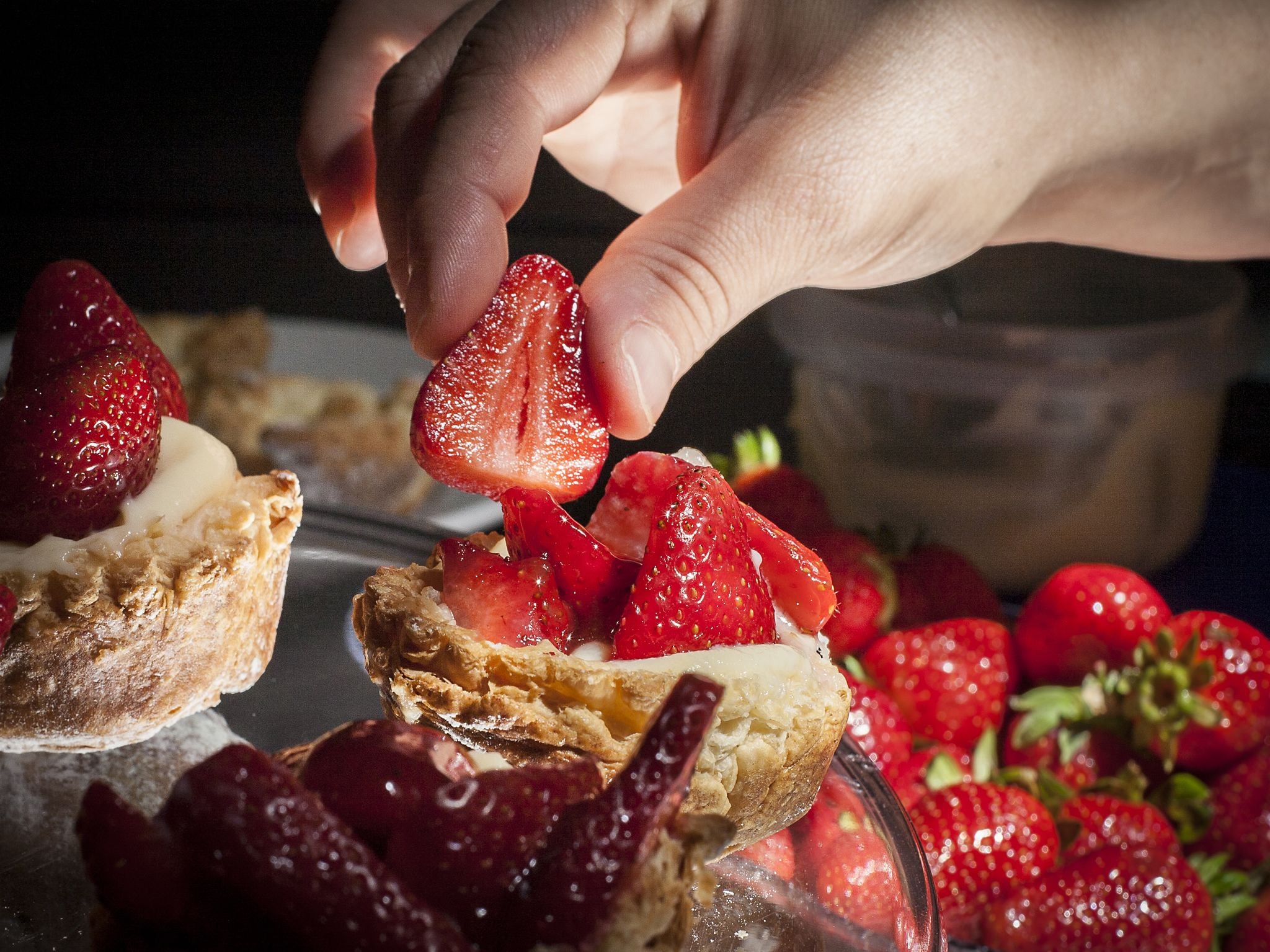 Una mano che tiene una fragola, circondata da fragole e da un dolce.