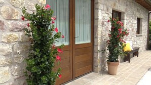 A stone building with a wooden door and windows, a bench, and potted plants with flowers. - Hotel Ideale (Assisi)