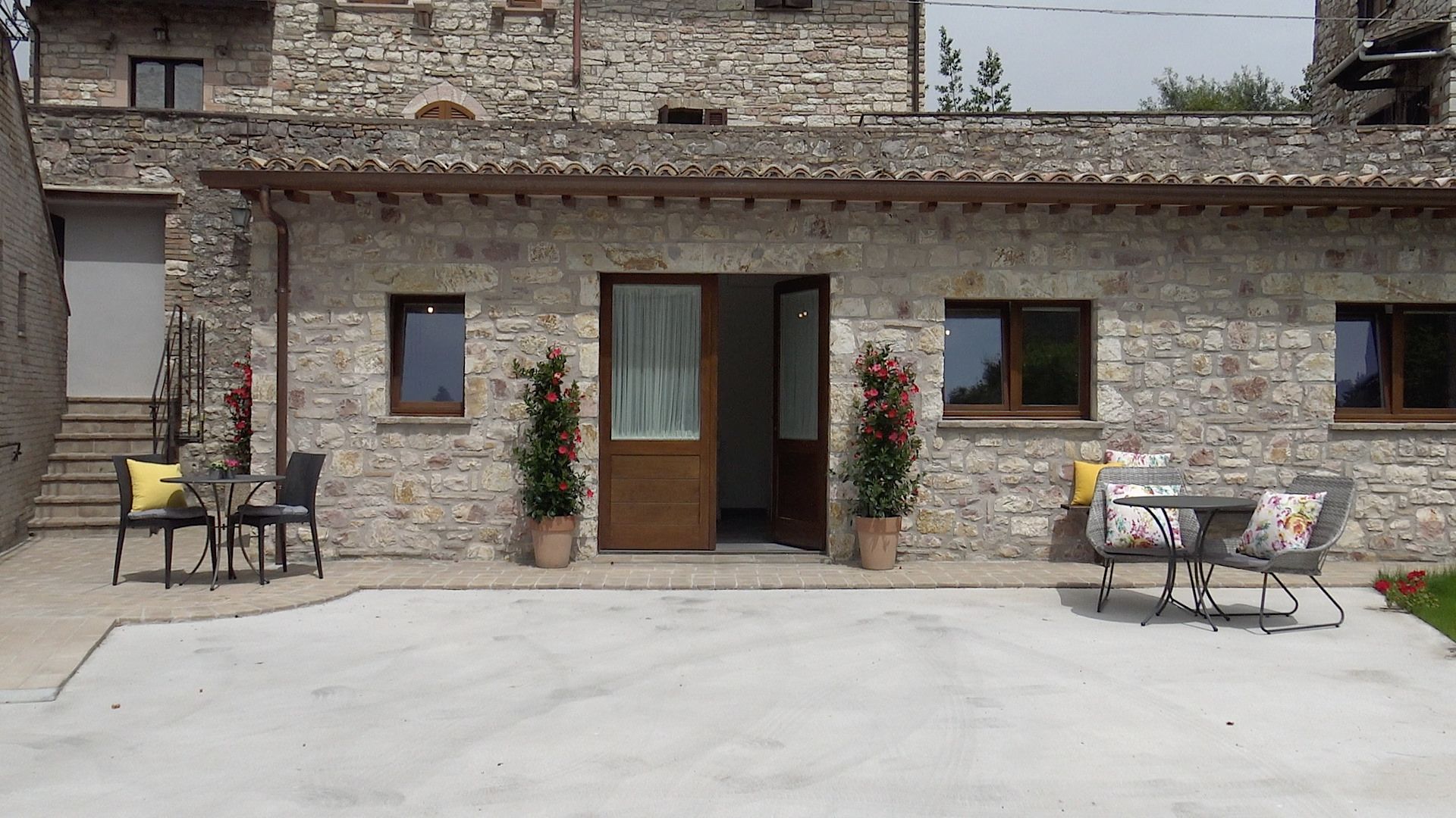 A stone building with a tiled roof, a wooden door, and a small porch area with outdoor furniture.