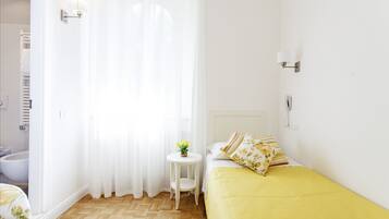 Ein Hotelzimmer mit Bett, einem kleinen Tisch mit Blumenvase, einem Badezimmer mit Badewanne und einer weißen Wand mit einer Leuchte.