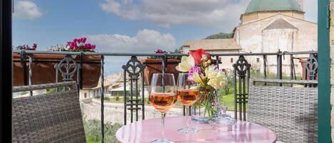 A balcony with wicker furniture, two glasses of wine, and a vase of flowers.