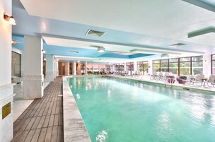 Una piscina techada, una piscina al aire libre, sombrillas