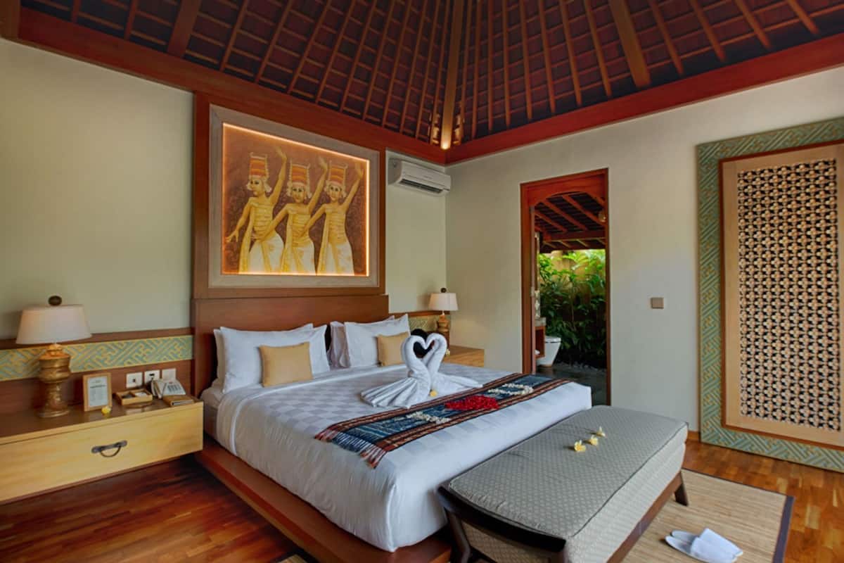 A hotel room with a bed, bedside tables, a wall-mounted air conditioner, and a decorative painting.