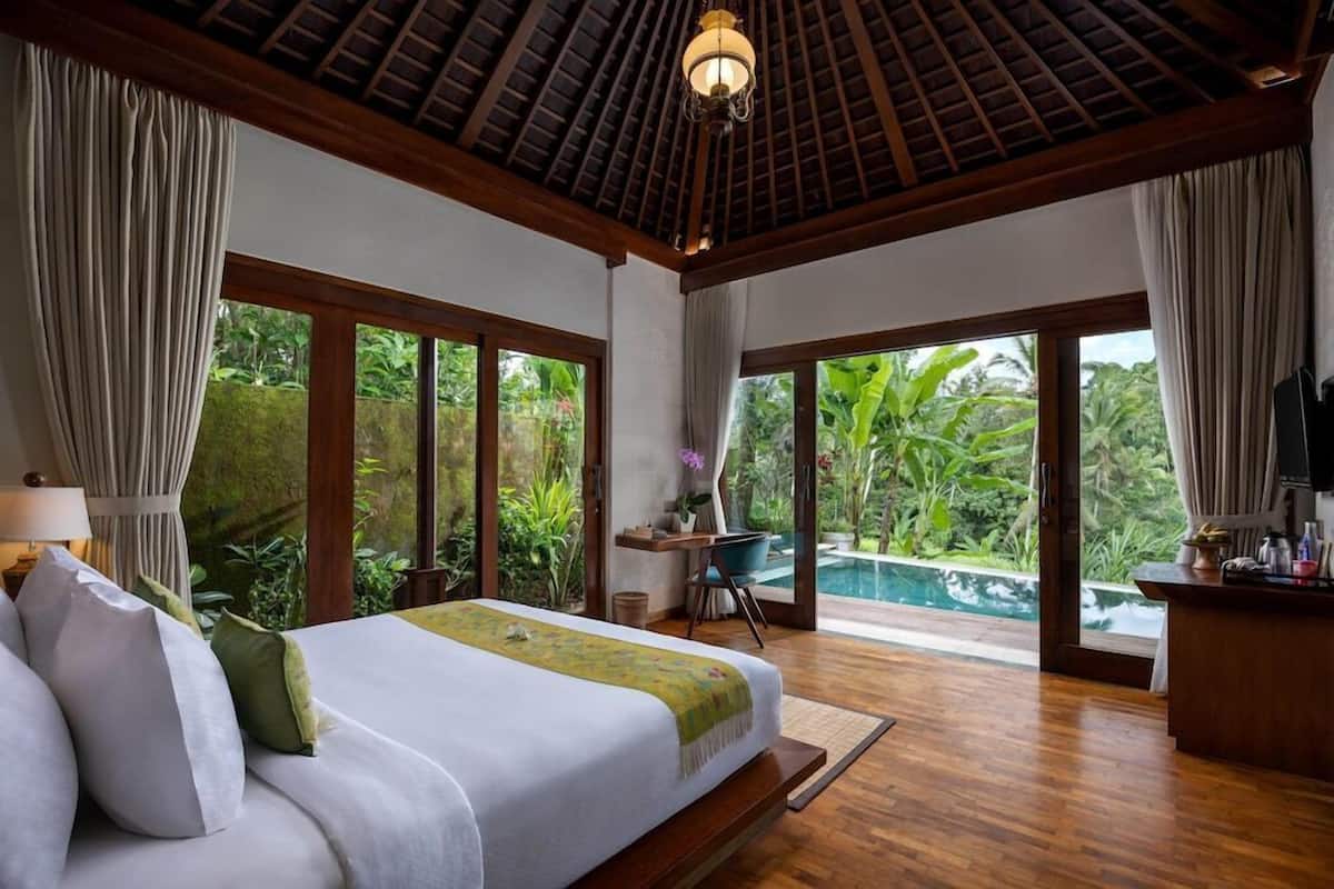 A bedroom with a bed, a desk, a chair, and a view of a swimming pool.