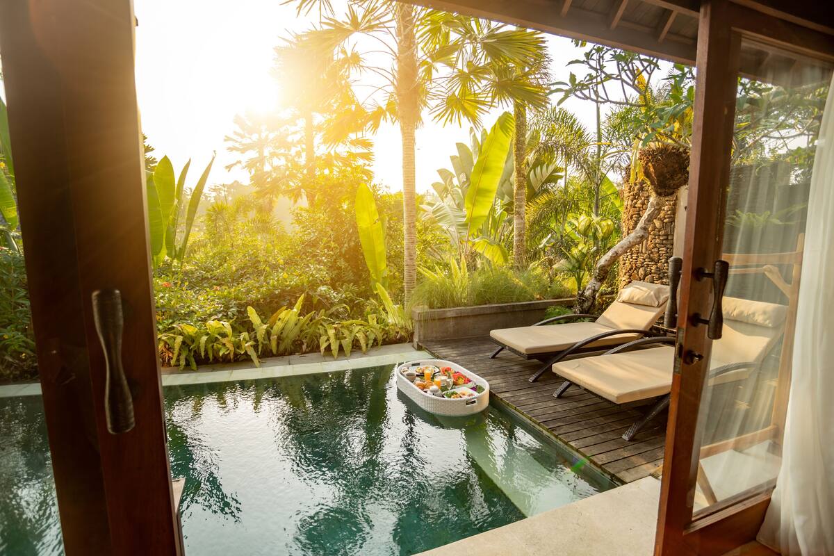 An outdoor pool area with lounge chairs, a floating bar, and lush tropical vegetation.