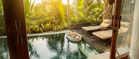An outdoor pool area with lounge chairs, a floating bar, and lush tropical vegetation.