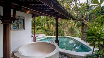 A spa area with a large hot tub and a swimming pool surrounded by lush greenery.