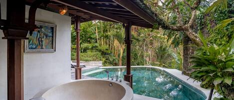 Un área de spa con un amplio jacuzzi y una piscina rodeada de exuberante vegetación.