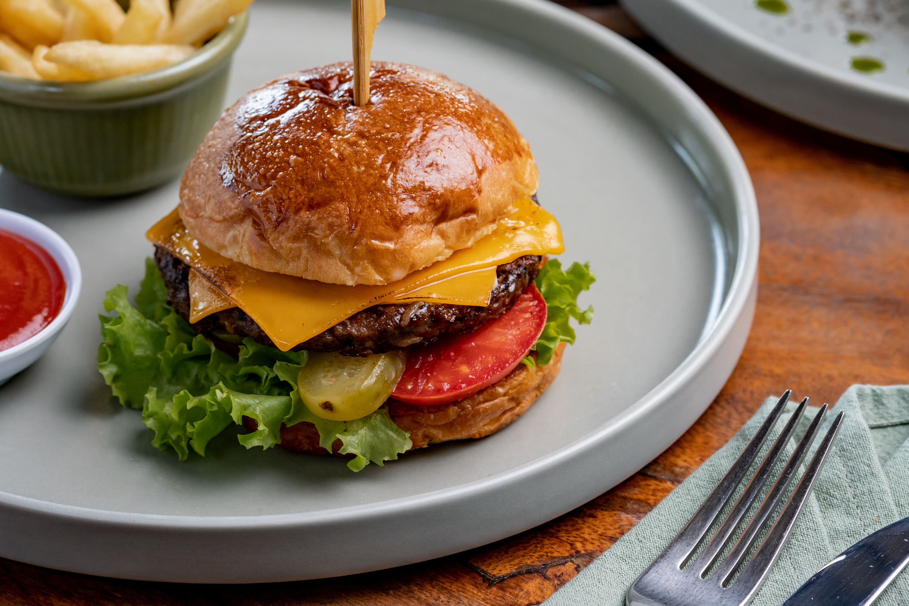 A burger with a toothpick, lettuce, tomato, and cheese on a plate.