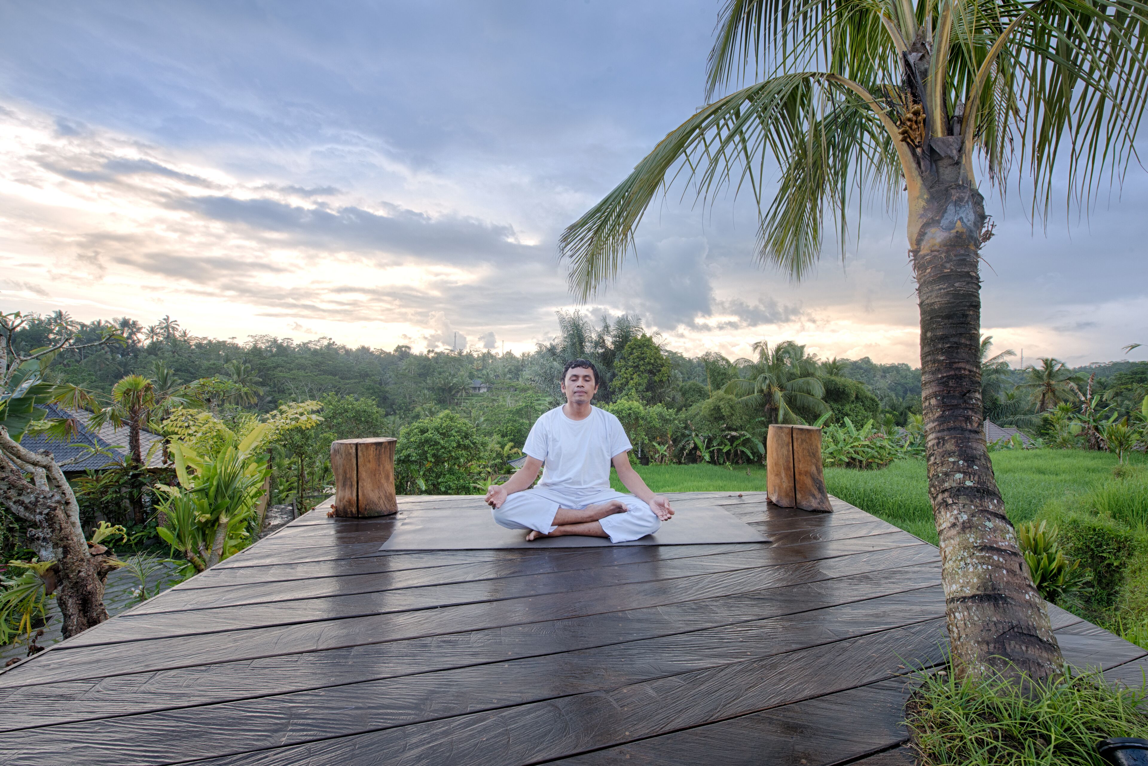 Una persona meditando en una terraza de madera, con un paisaje natural de fondo.