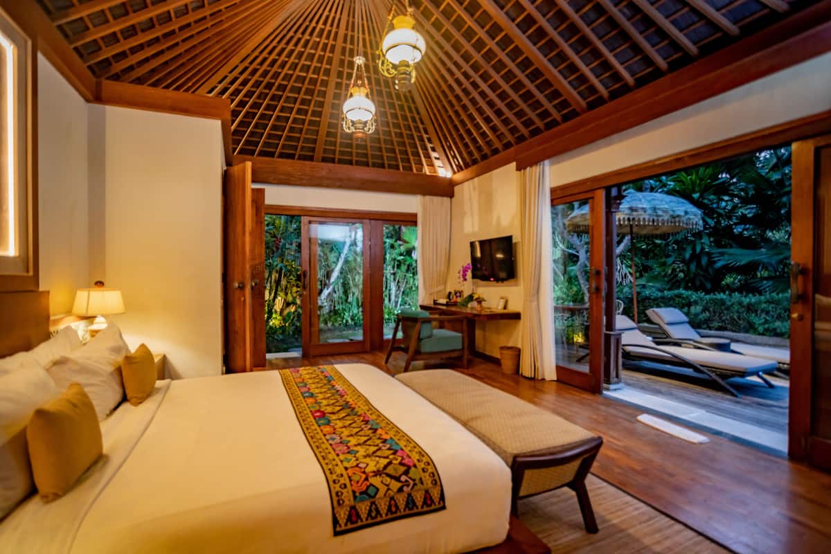 A spacious bedroom with a large bed, a desk, and a view of a lush garden through sliding glass doors.
